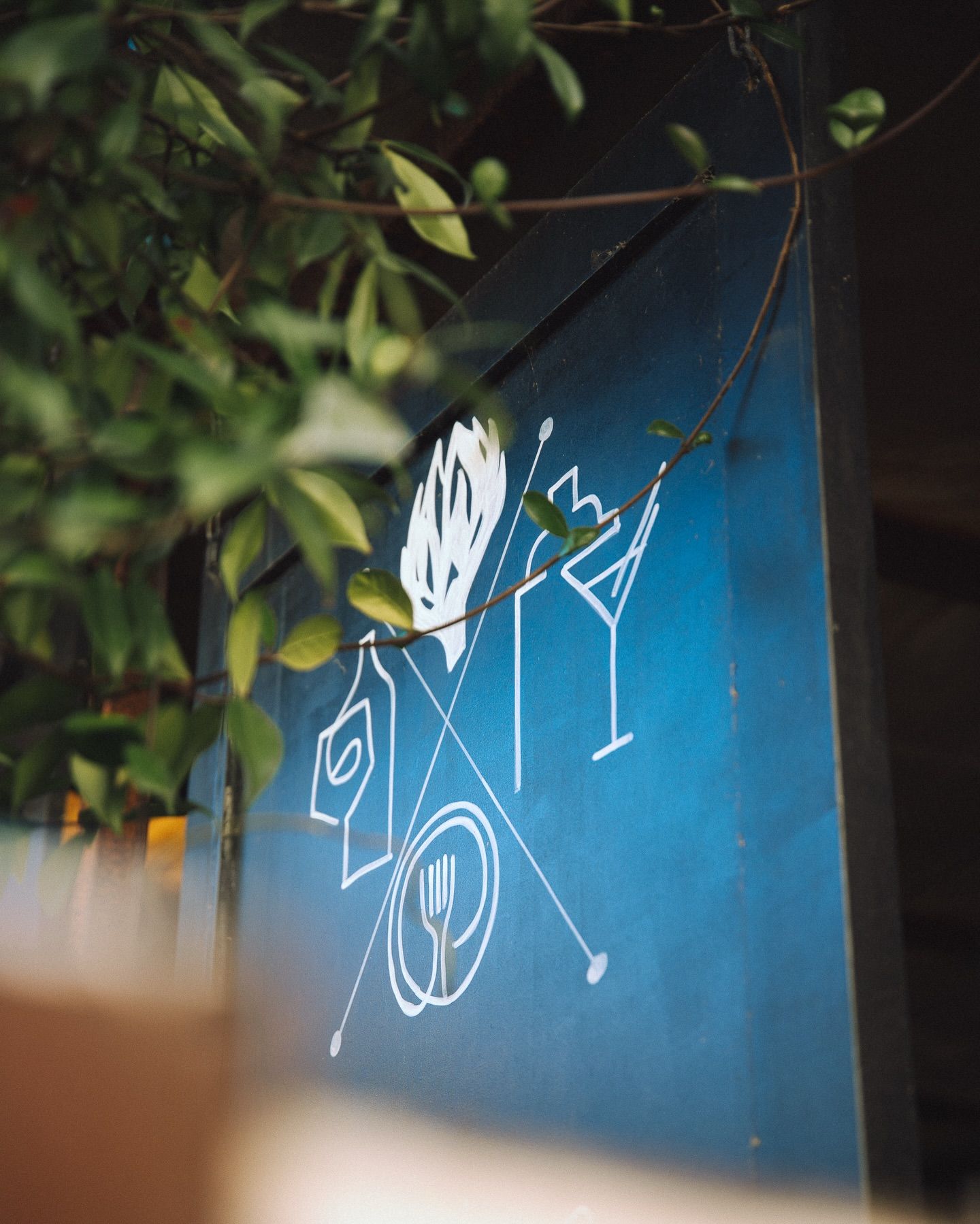 Un panneau bleu orné d'icônes blanches dessinées au trait représentant une bouteille, une flamme, une fourchette, une assiette et un verre à cocktail