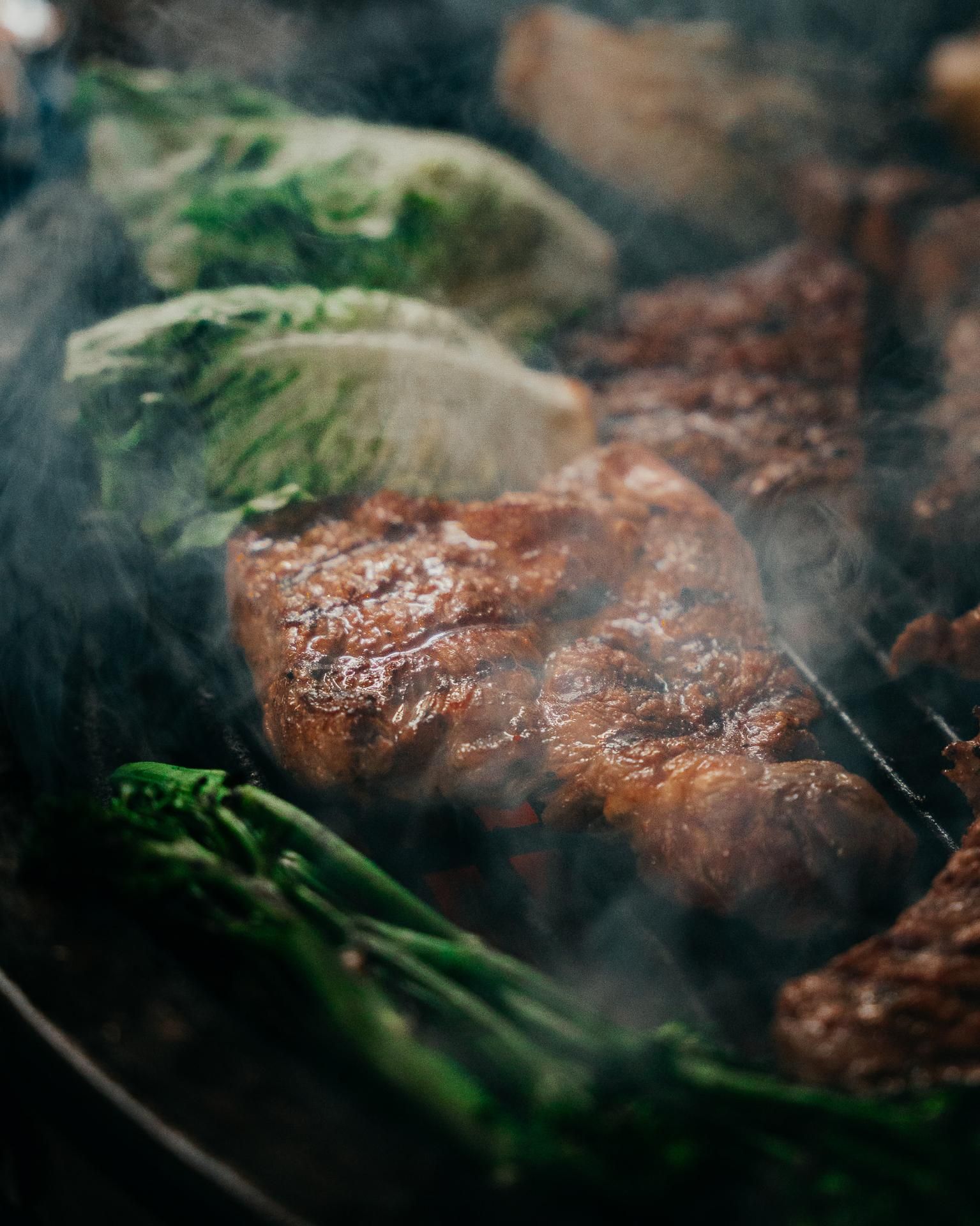 Gros plan sur un steak, de la laitue et des légumes verts grillés sur une flamme nue, avec de la fumée