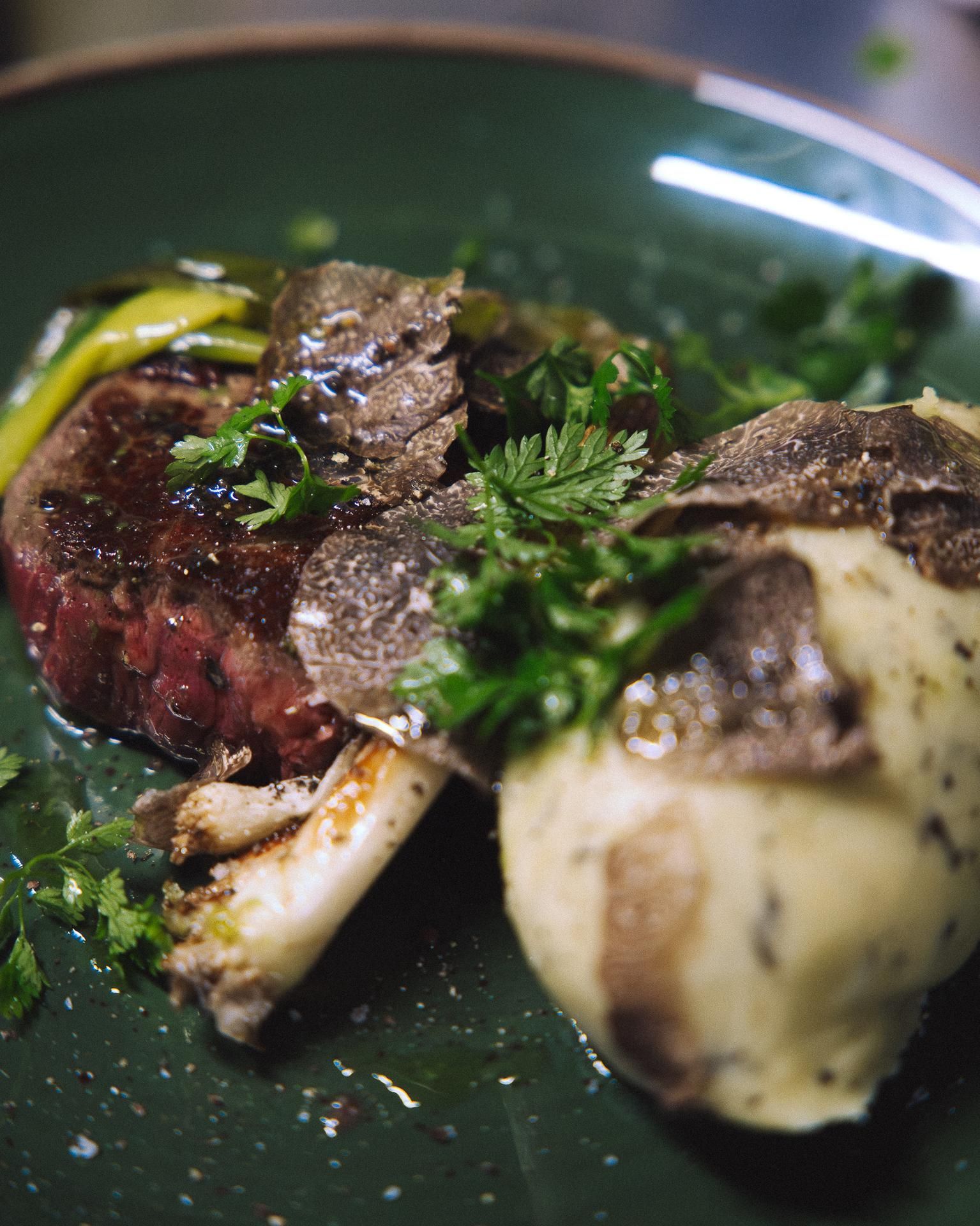 Une assiette gourmande composée d'un steak saisi, de purée de pommes de terre et d'herbes fraîches, garnie de fines tranches de truffes noires
