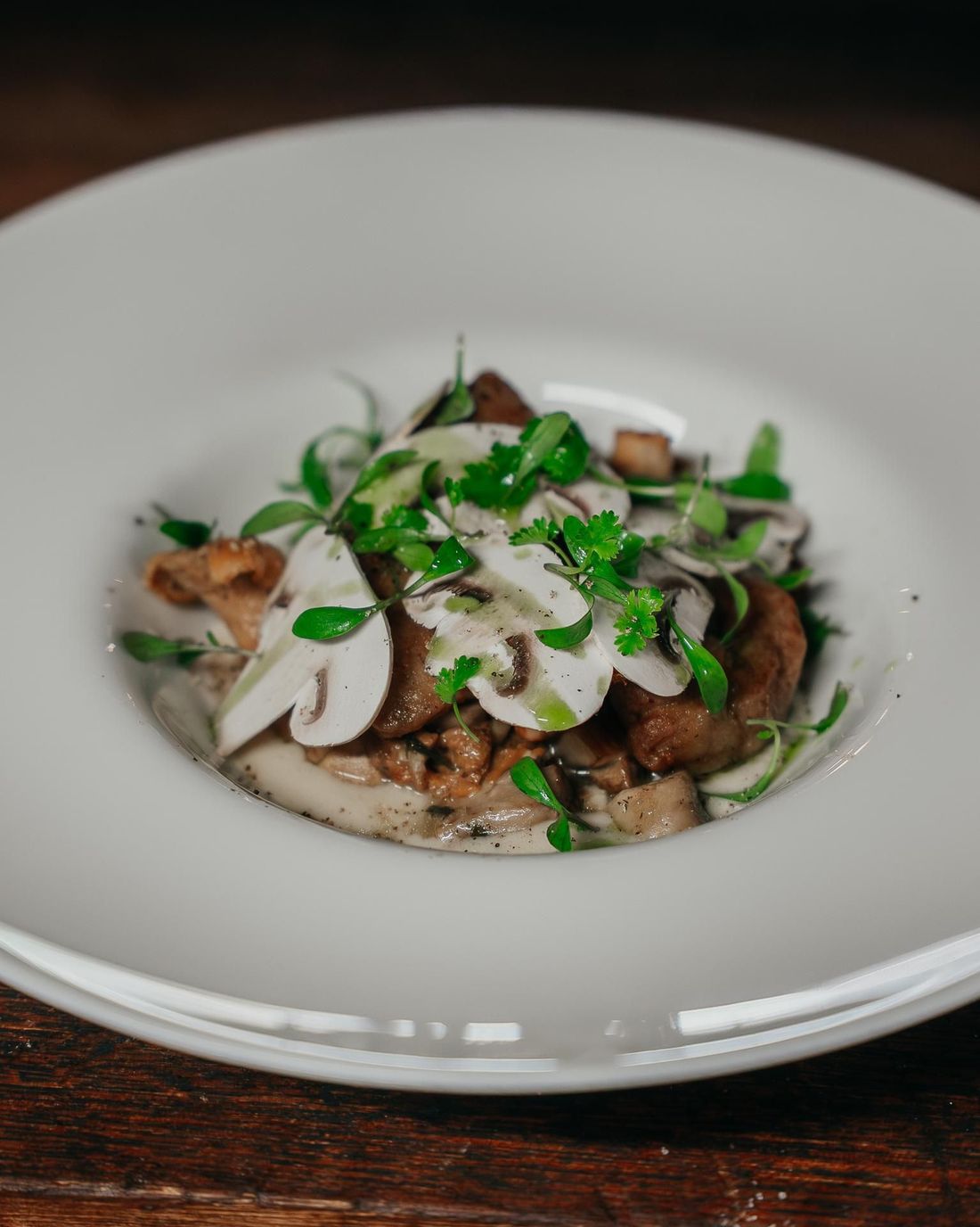 Un plat gastronomique de champignons sautés, garni de fines tranches de champignons crus et d'herbes fraîches, servi sur une assiette blanche