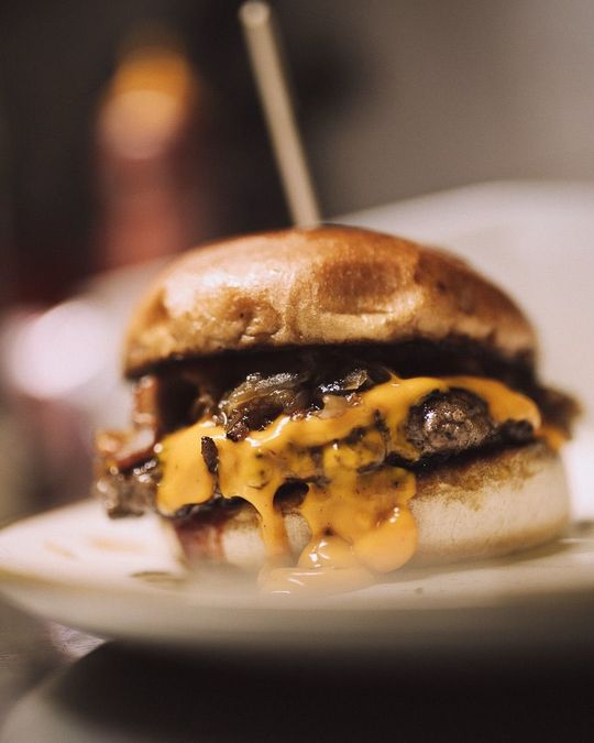 Un cheeseburger avec du fromage jaune fondu et des oignons sautés, le tout servi dans un pain brioché et maintenu par un cure-dent en bois sur une assiette blanche