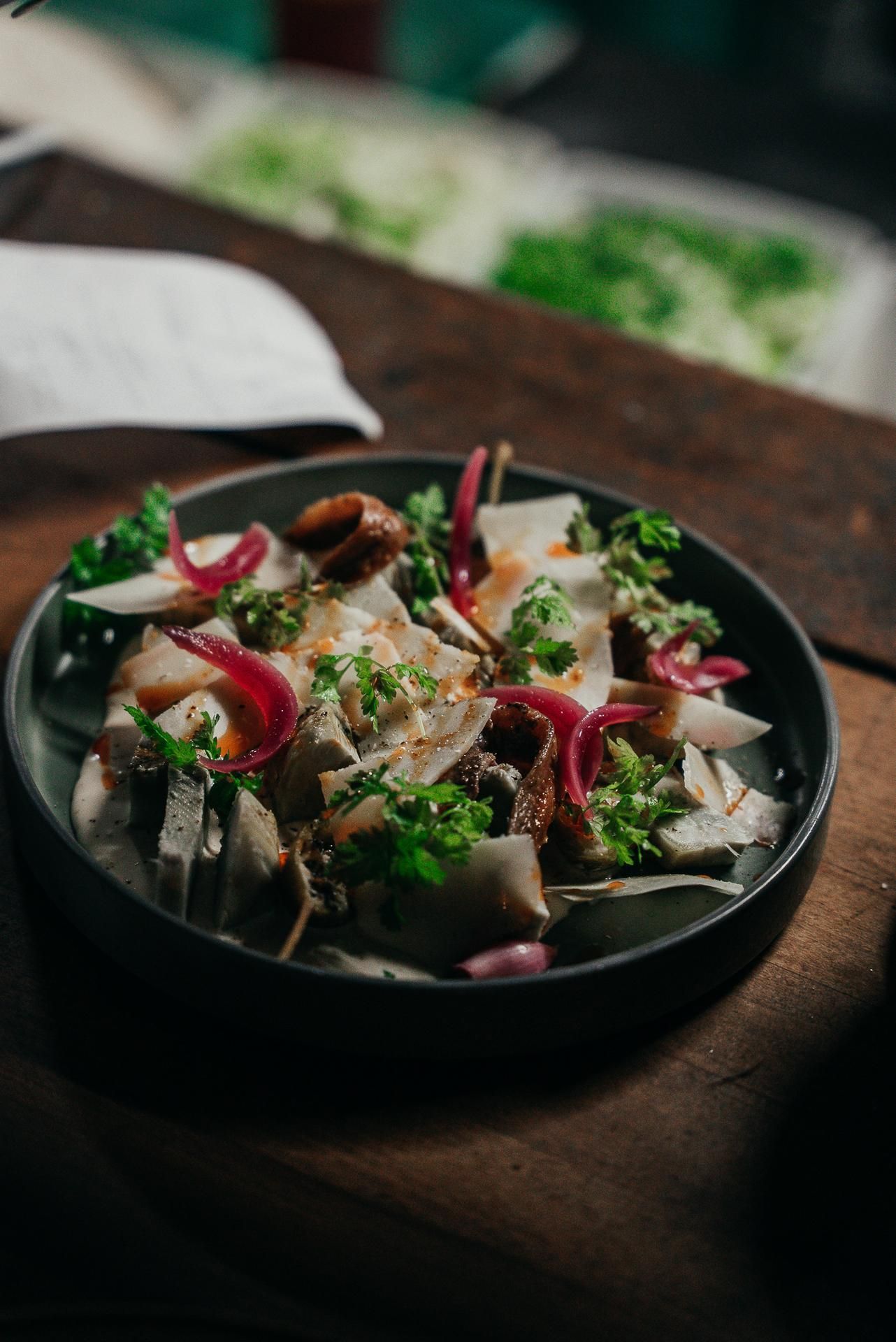 Une salade gourmande avec du parmesan râpé, des oignons rouges et des herbes fraîches, servie dans un saladier sombre sur une table rustique en bois
