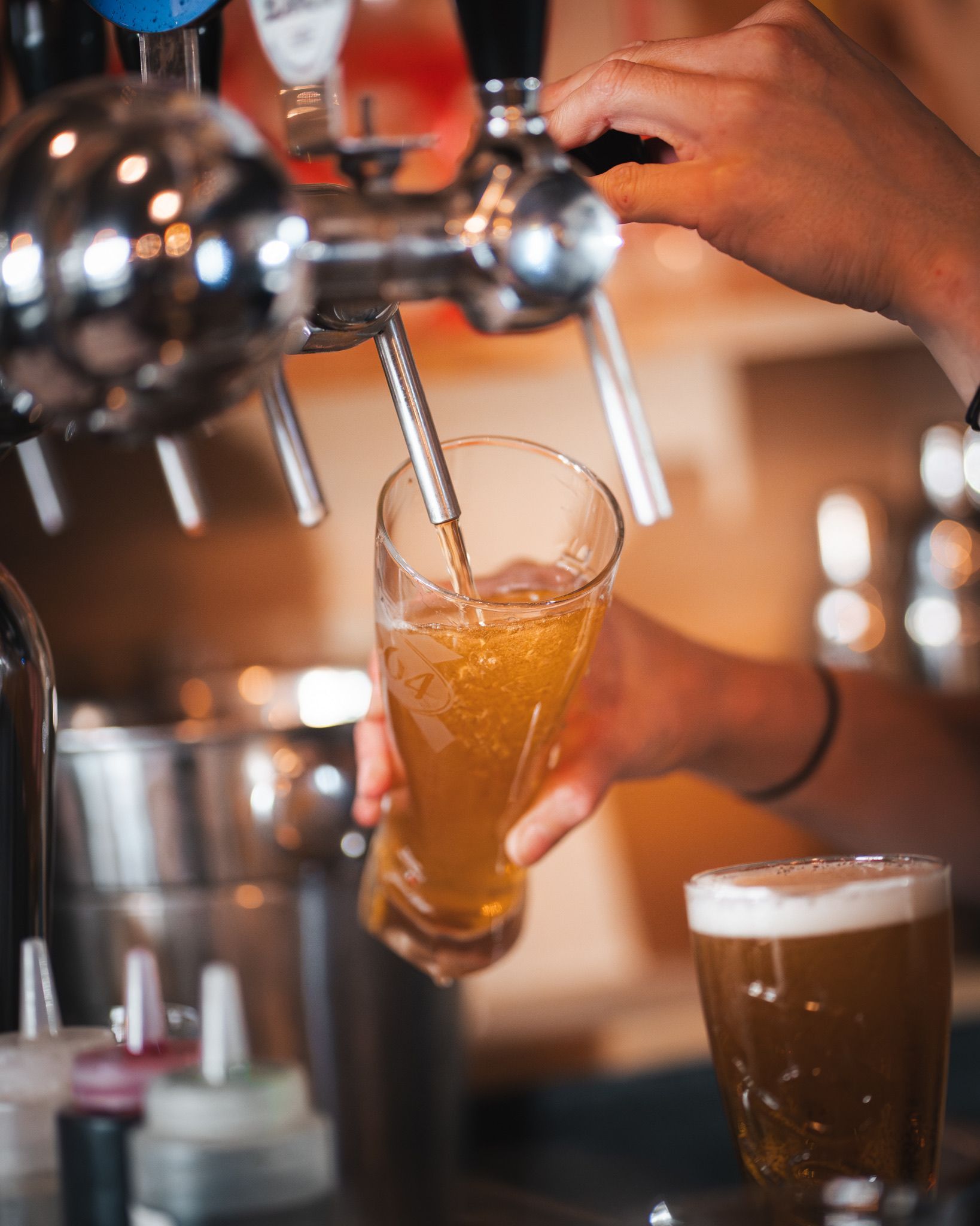 Un barman verse une bière pression dans un grand verre, tandis qu'un verre de bière plein est posé sur le comptoir à proximité