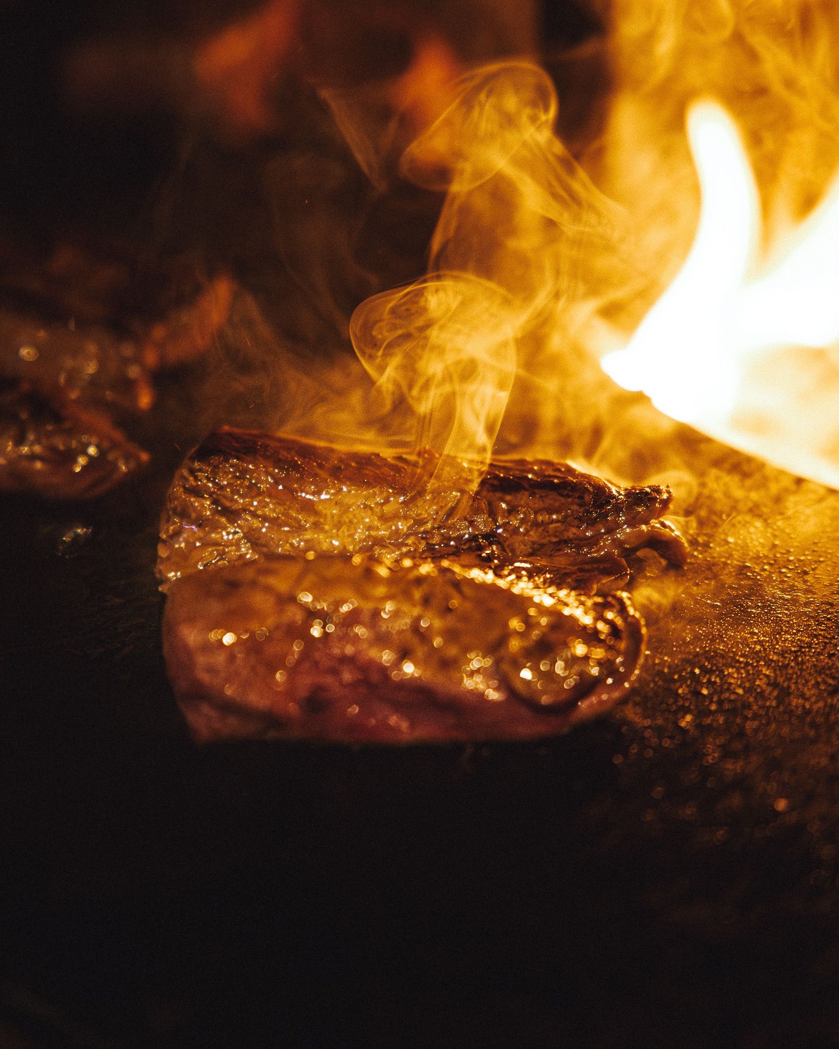 Un morceau de steak qui cuit sur un gril brûlant, avec des flammes visibles et de la fumée qui s'en dégage