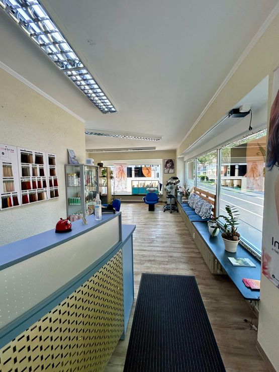 Helles Saloninterieur mit Nagellackdisplays, blauen Sitzmöbeln und einem gestreiften Läuferteppich.