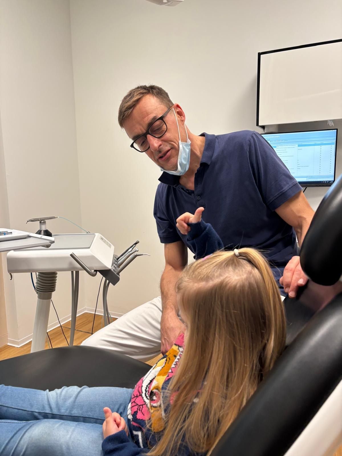 Kind beim Zahnarzt, Mund geöffnet, zur zahnärztlichen Untersuchung. Zahnarzt hält Instrumente, trägt Handschuhe.