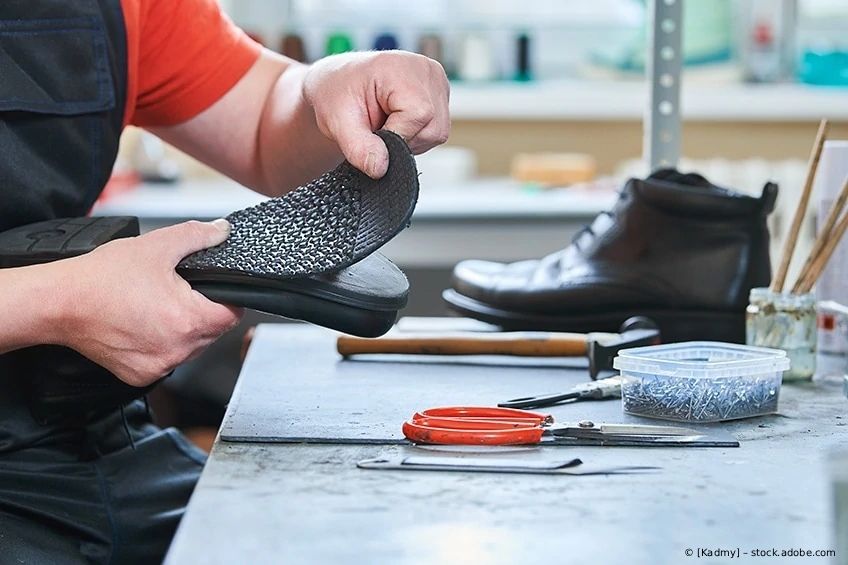 Person in Werkstatt prüft strukturierte Schuhsohle neben Werkzeugen.