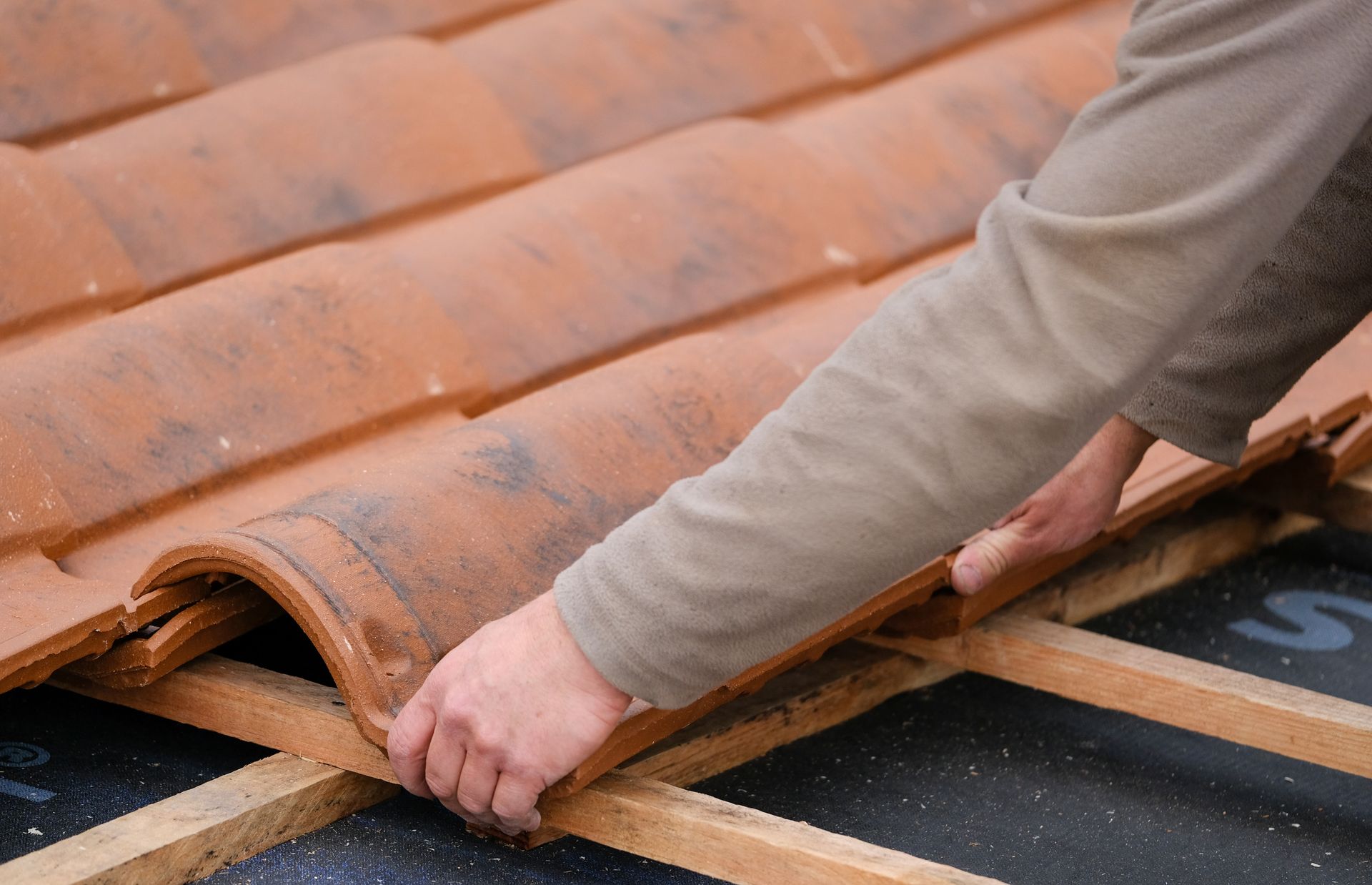 Des mains ajustent des tuiles orange sur le toit d'une maison en réparation