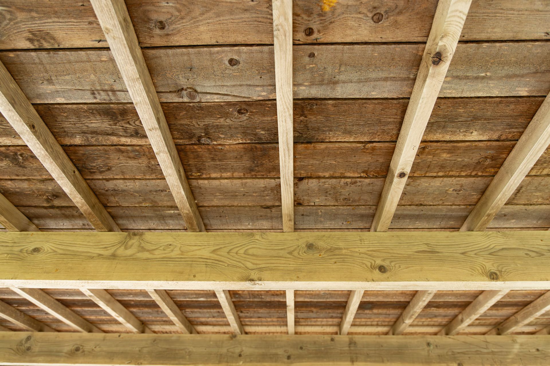 Solives et poutres de plafond en bois vues d'en bas, avec planches et isolation apparentes.
