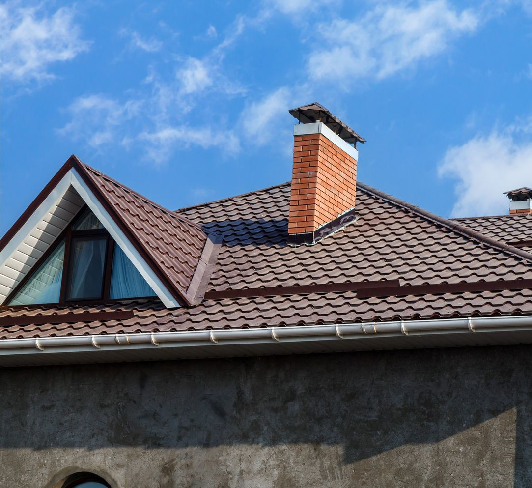 Toit de maison en tuiles brunes, cheminée en briques et ciel bleu parsemé de nuages