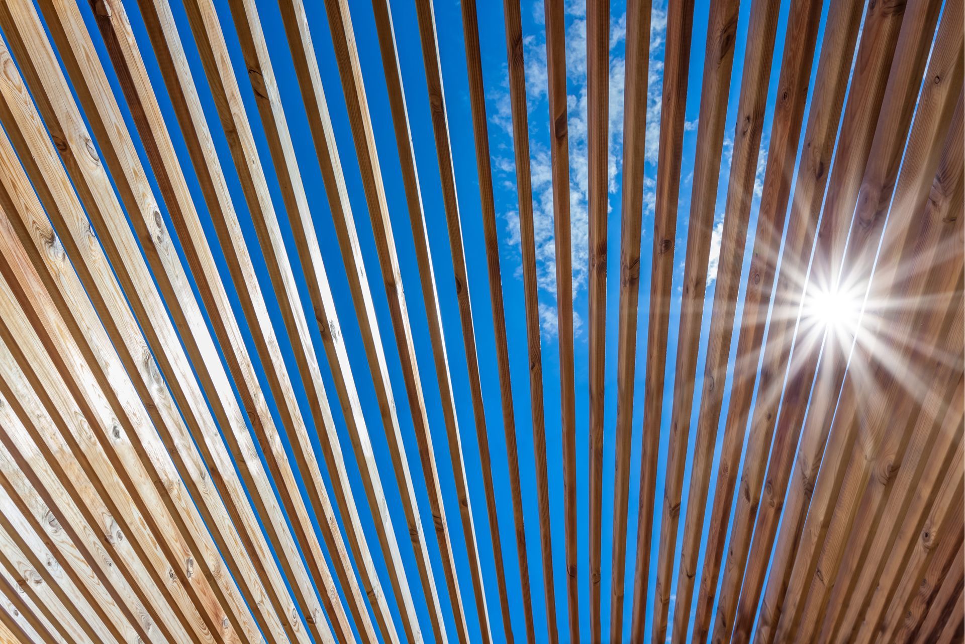 Ciel bleu aperçu à travers des lattes de bois, illuminé par un éclat de soleil.