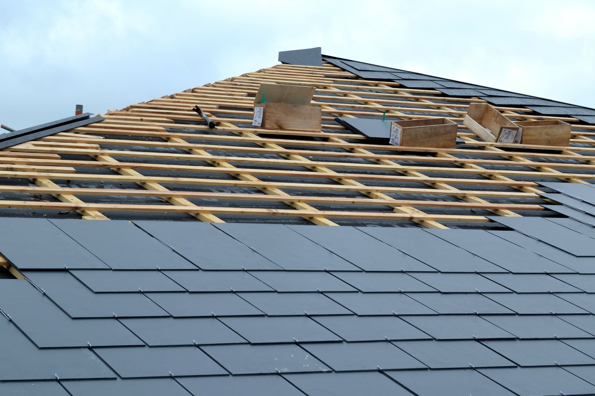 Toiture en construction avec charpente en bois apparente et bardeaux gris partiellement posés.