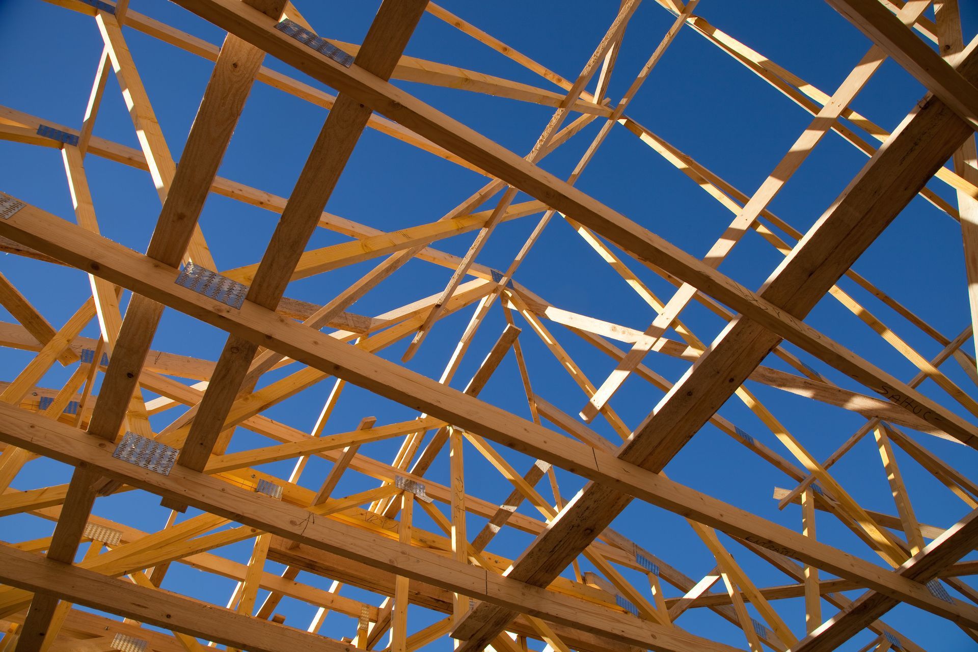 Charpente de toit en bois en construction, sur fond de ciel bleu clair.