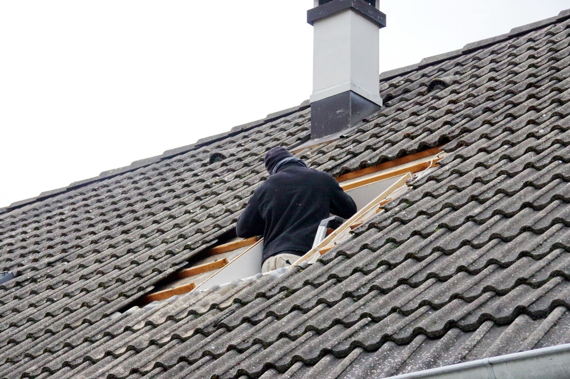 Une personne travaille sur un toit de tuiles près d'une cheminée, réparant une partie ouverte sous les bardeaux.