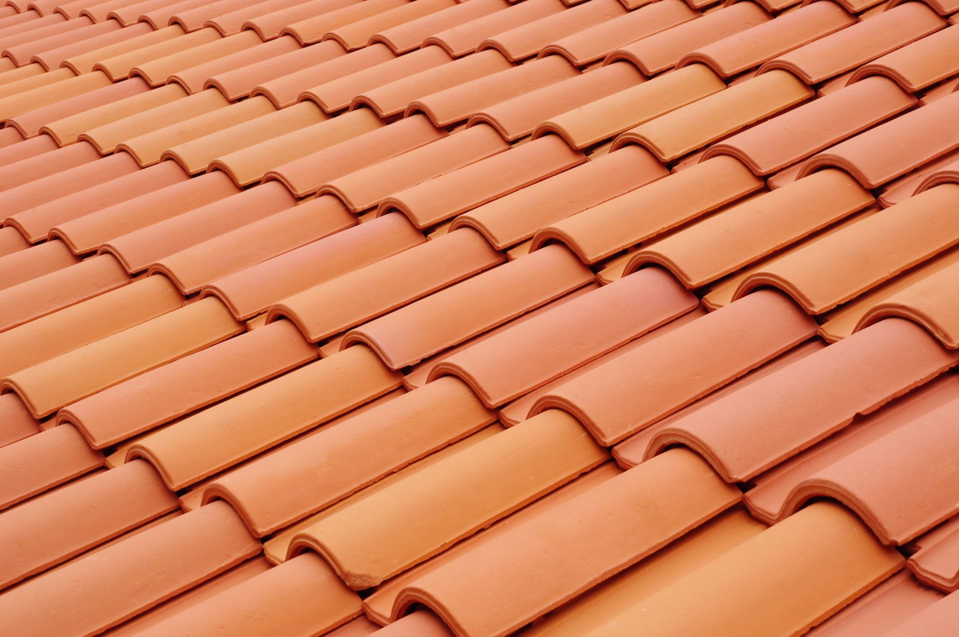 Gros plan sur des tuiles de toit en terre cuite orange, disposées en rangées régulières et superposées.