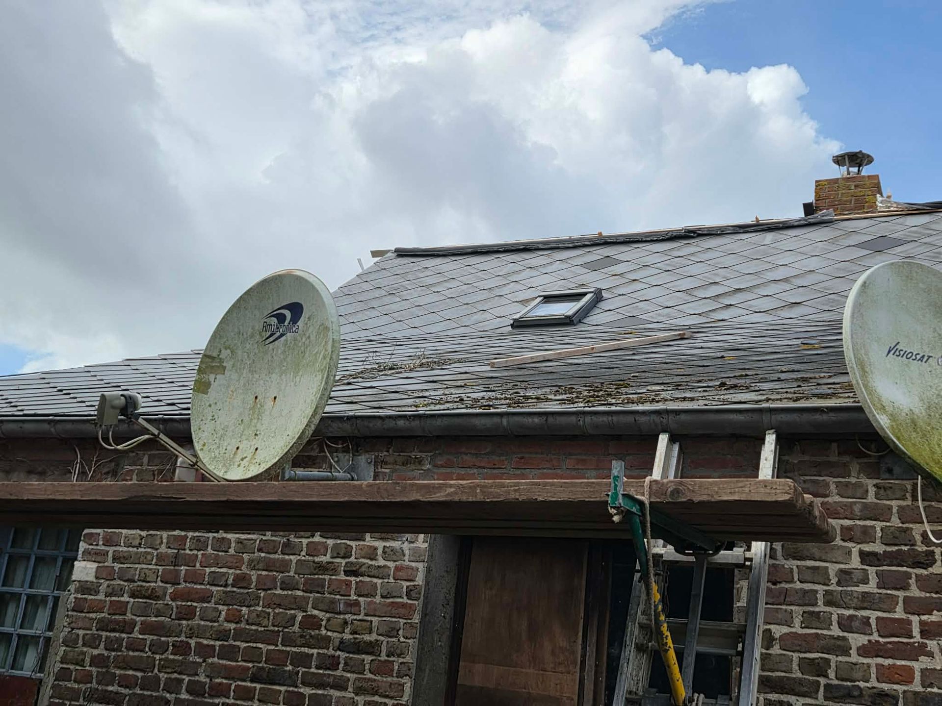 Toit de maison en pierre avec deux antennes paraboliques sous un ciel nuageux