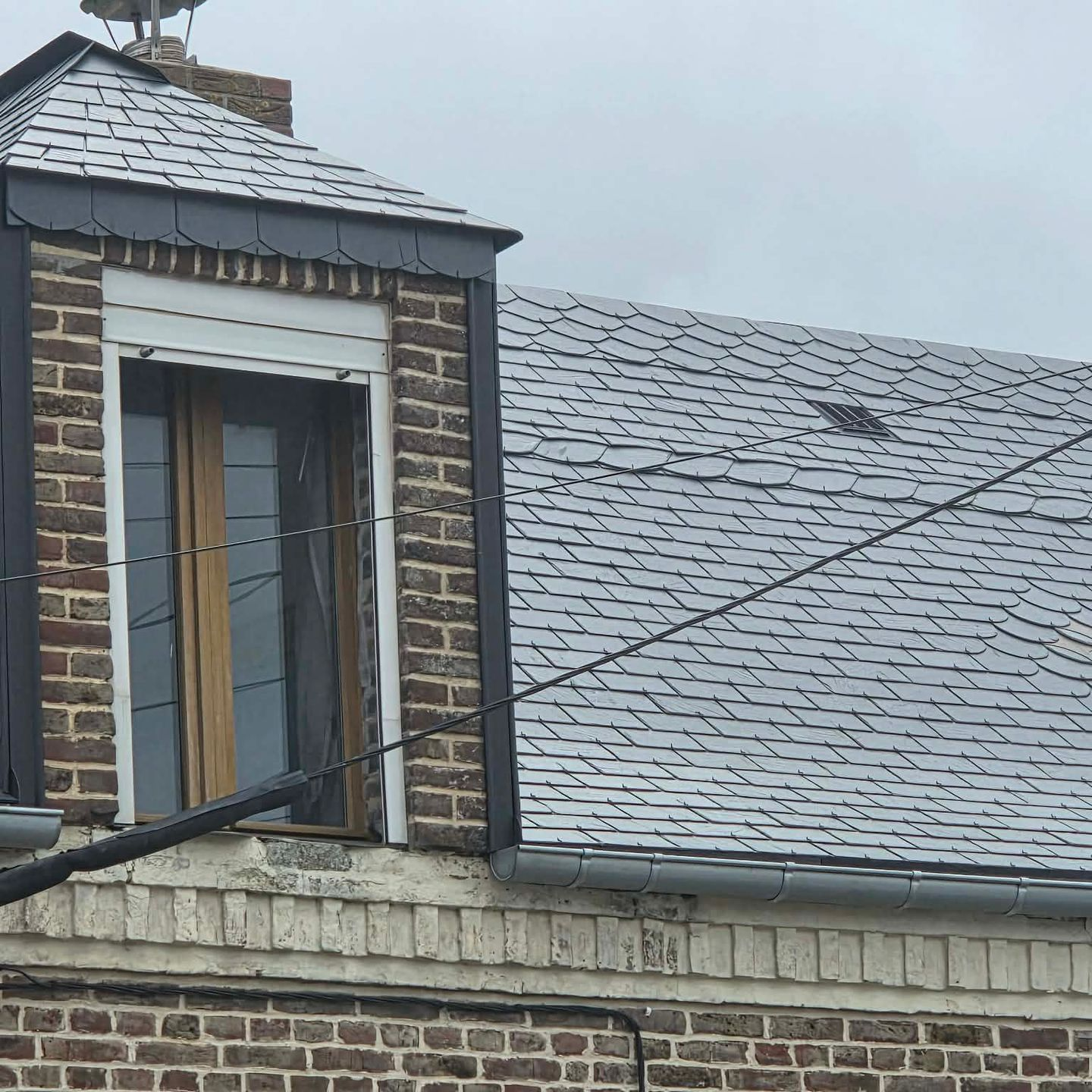 Toit de maison en briques recouvert d'ardoises grises et d'une lucarne par temps couvert