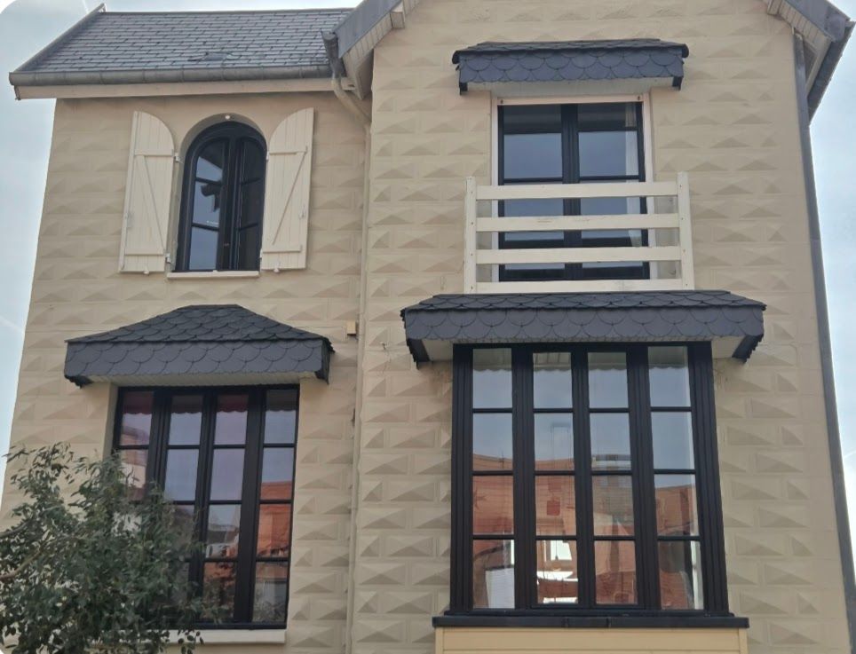 Façade de maison à deux étages en stuc beige avec fenêtres à cadre foncé et auvents noirs