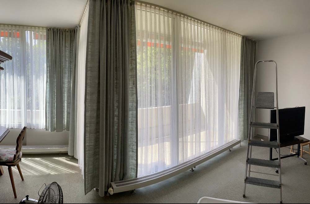 Ein Wohnzimmer mit großem Fenster und Vorhängen und einer Leiter.