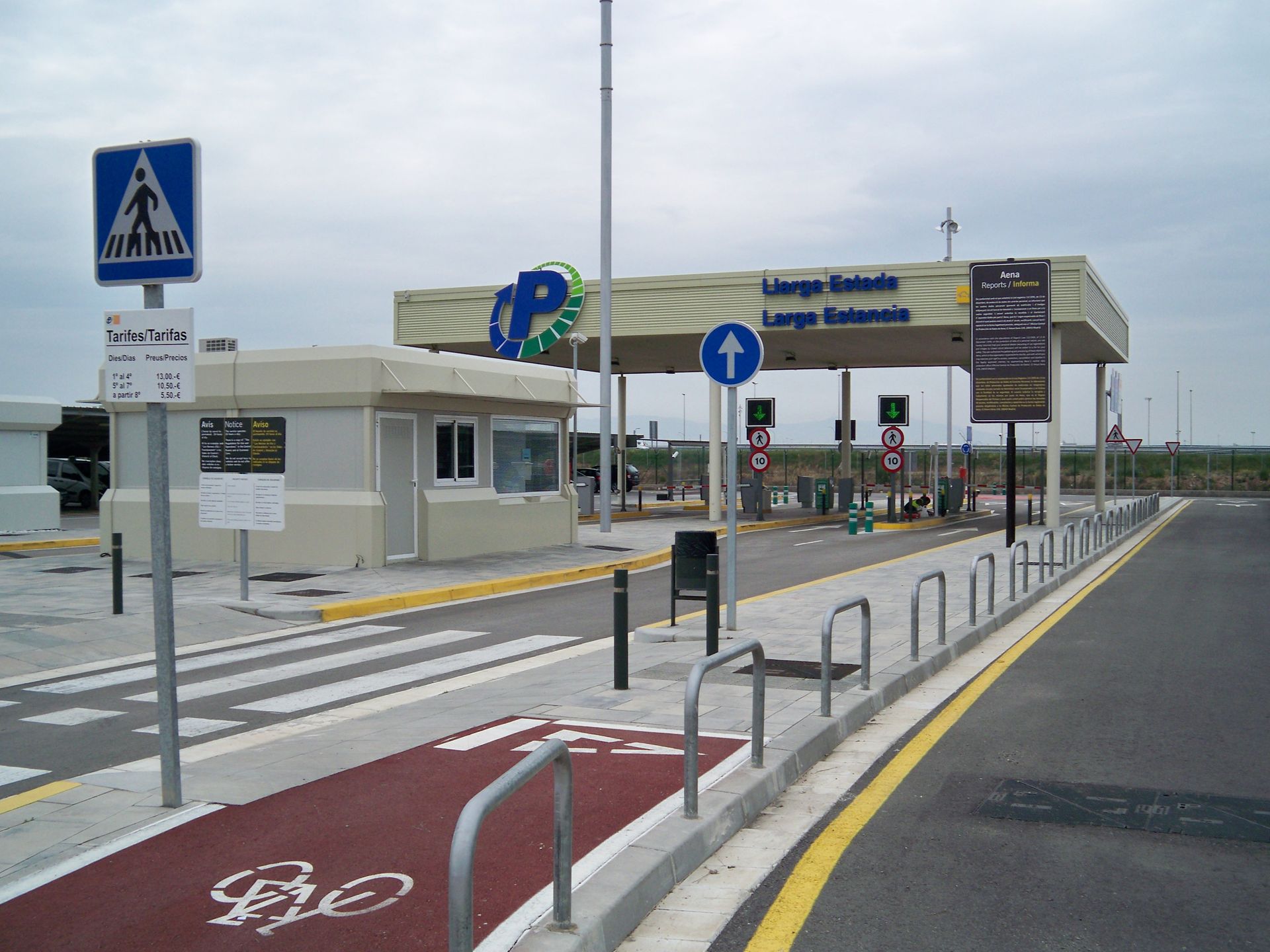Cabina de peaje con paso de peatones, carril bici y carriles de pago; cielo nublado.