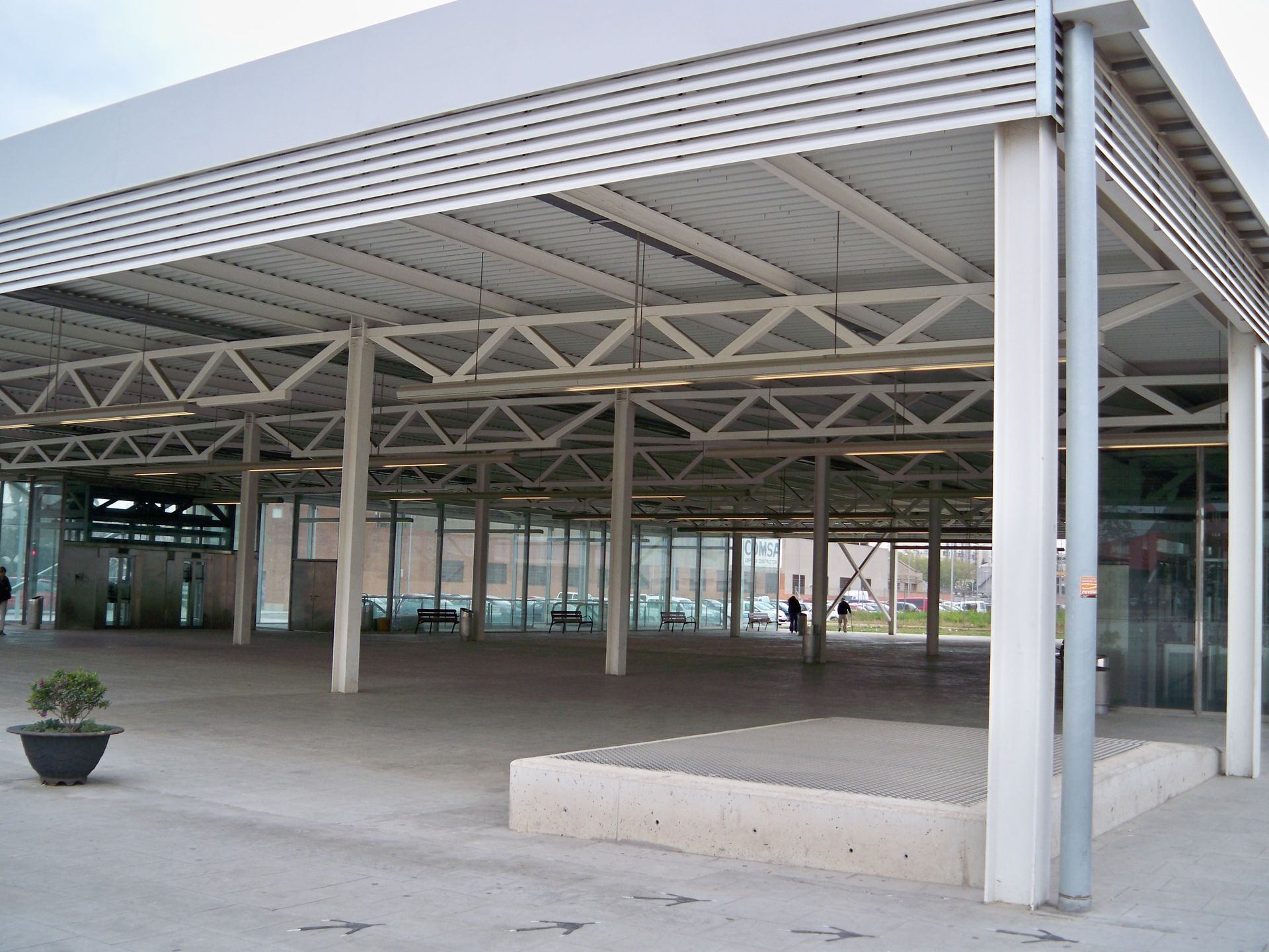Un espacio público cubierto con vigas blancas, pilares y suelo de hormigón.