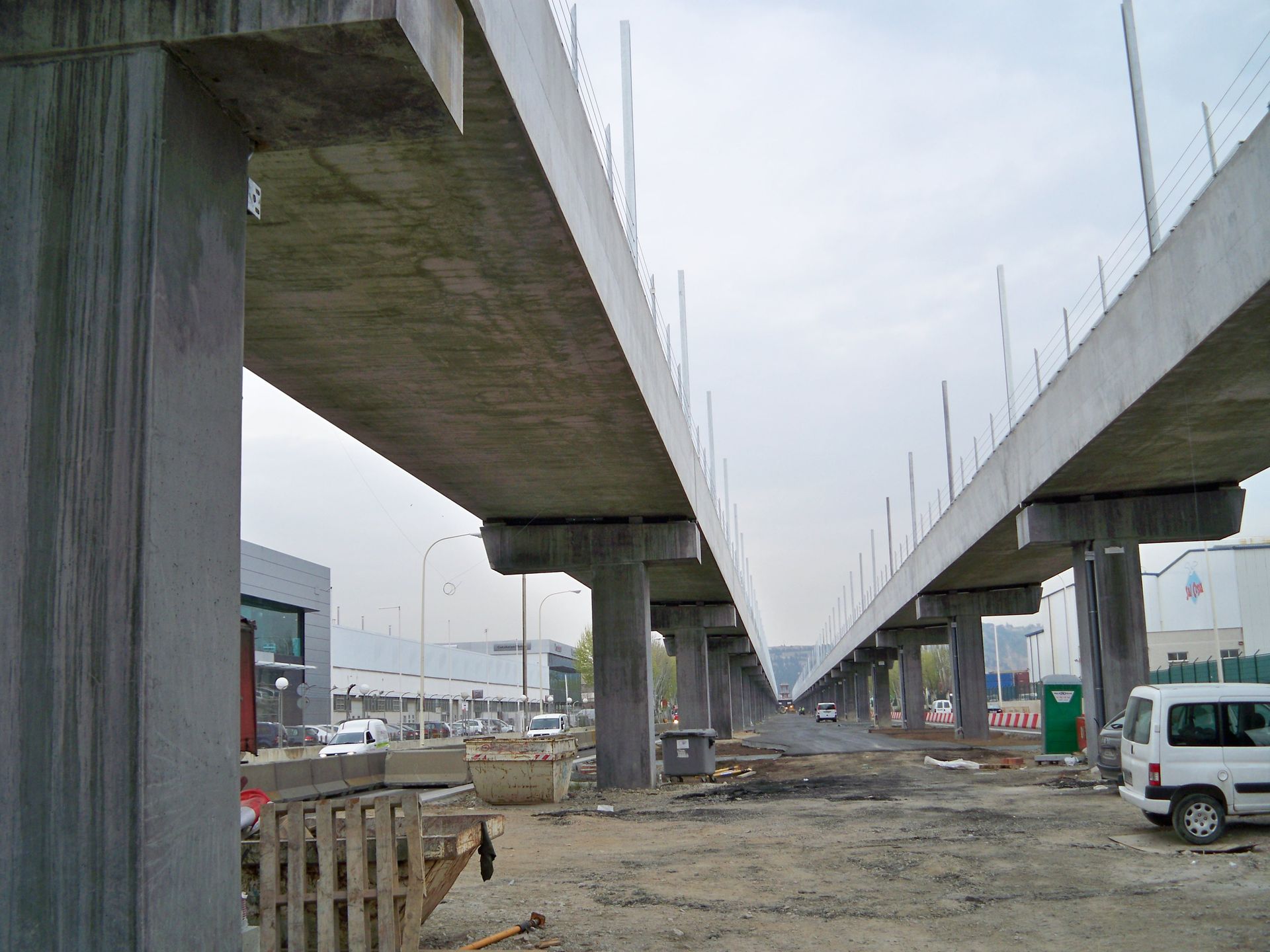 Vías de tren elevadas en construcción, sostenidas por pilares de hormigón, en una zona urbana.