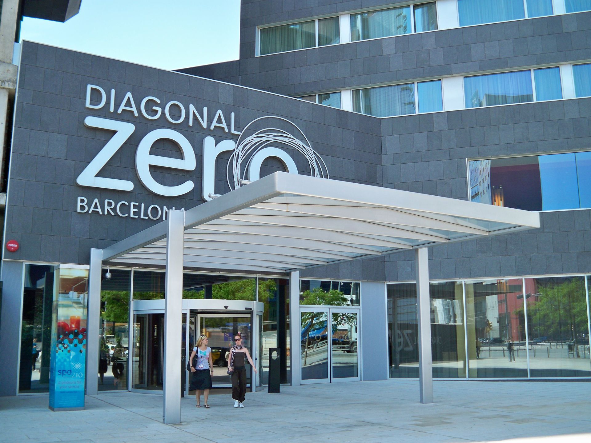 Entrada del hotel Diagonal Zero de Barcelona con dos personas caminando hacia las puertas.