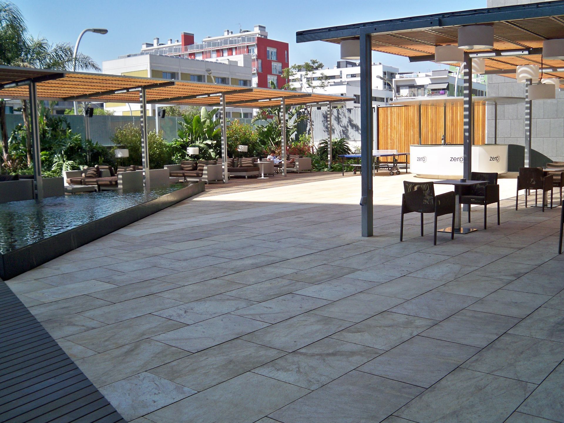 Patio al aire libre con piso de piedra, asientos, estructuras de madera y un estanque reflectante.