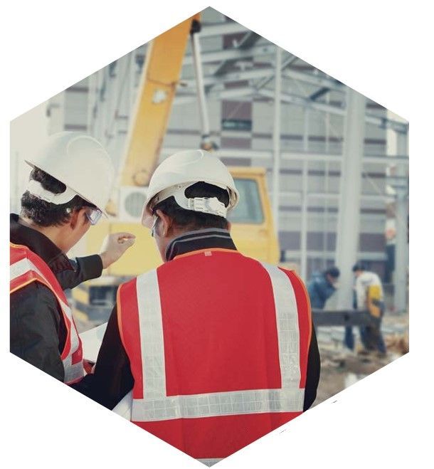 Dos trabajadores de la construcción con chalecos rojos y cascos blancos discuten planes en una obra en construcción.