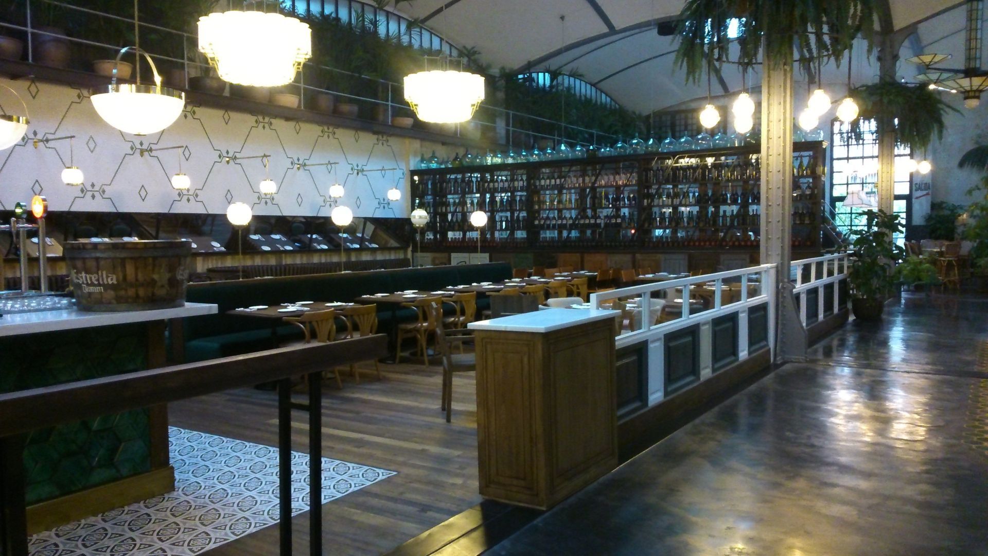 Interior del restaurante con suelos de madera, mesas e iluminación. Se aprecian zonas verdes y una zona de bar.