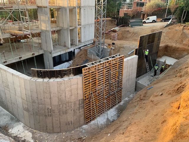 Obra en construcción con muros de hormigón, encofrado de madera y obreros.