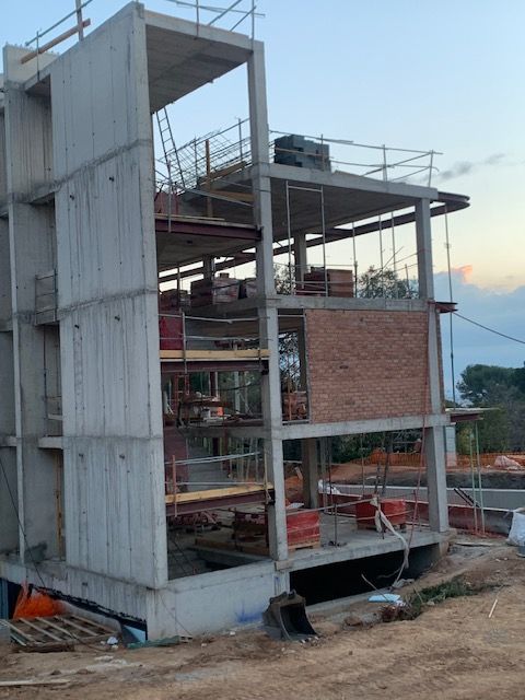 Edificio en construcción con estructura de hormigón, pared de ladrillo, andamios y materiales.