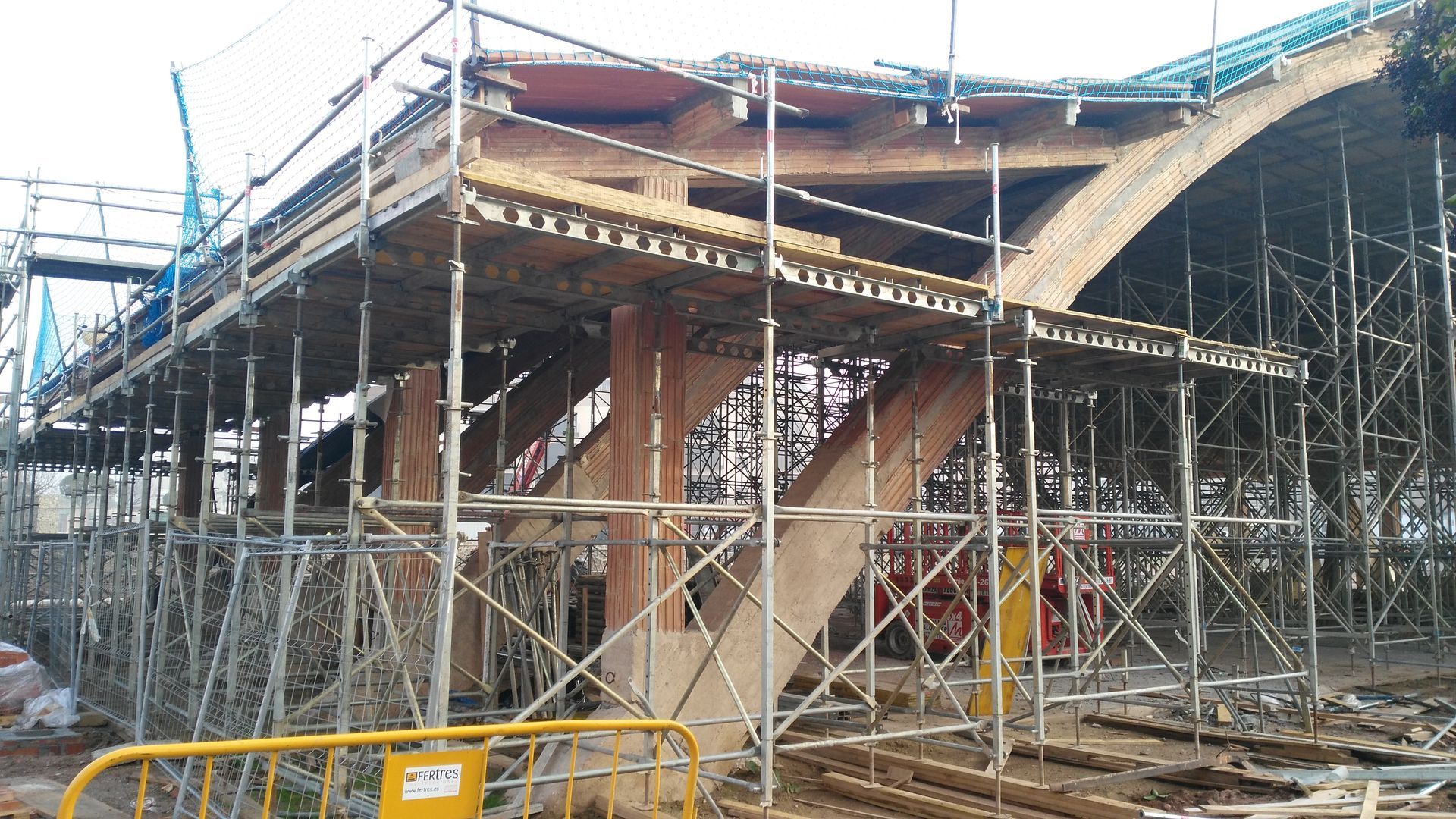 Obra de construcción con andamios que sostienen una estructura arqueada de madera.