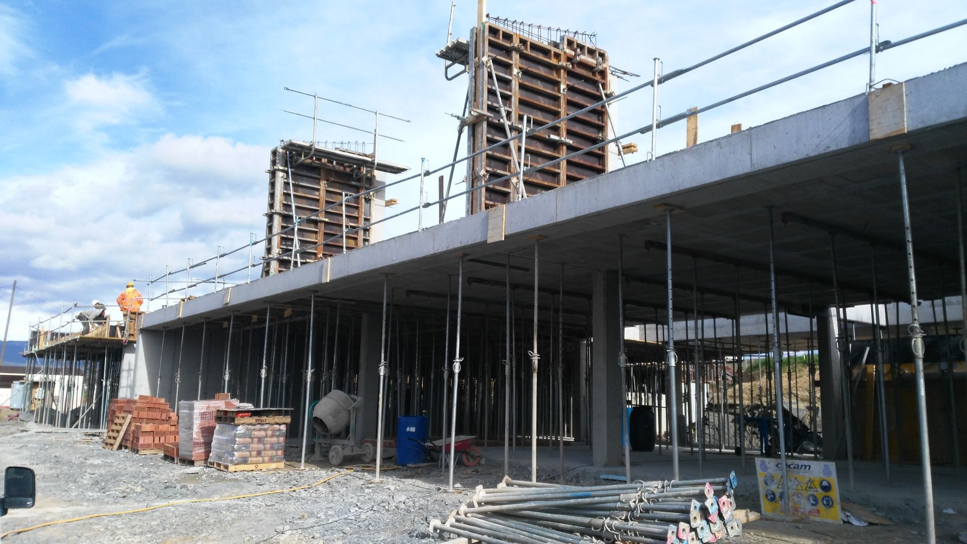 Sitio de construcción con encofrados de hormigón, trabajadores y vigas de soporte.