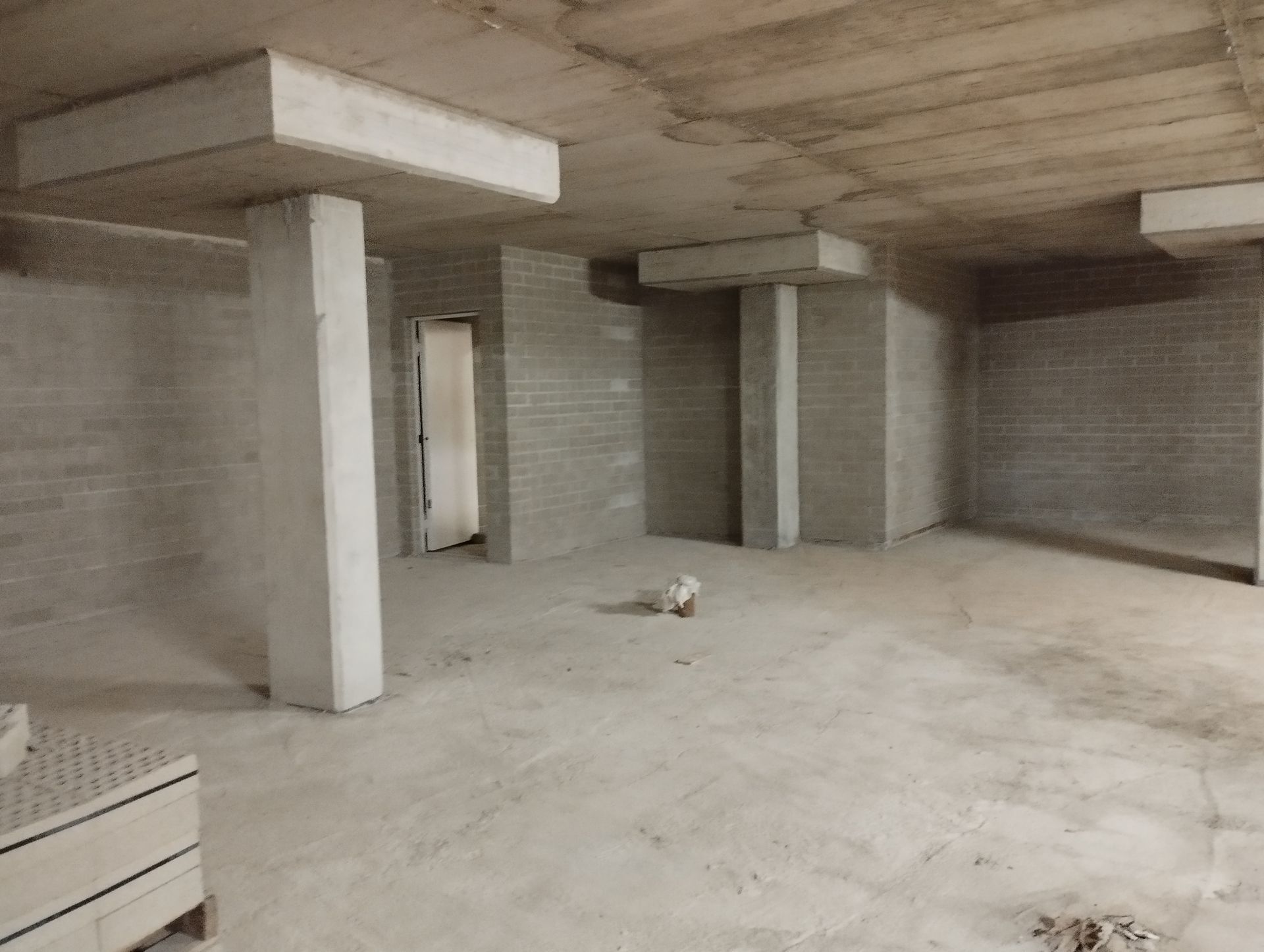 Interior de hormigón sin terminar con pilares, techo y puerta a la vista.