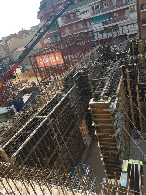 Obra en construcción con encofrados para muros de concreto, varillas de refuerzo visibles, grúa y el logo de “COPISA”.