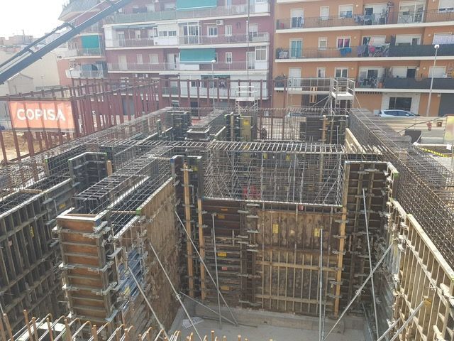 Sitio de construcción con encofrados de hormigón y estructura de varillas de refuerzo, probablemente para la cimentación de un edificio, en un área urbana.