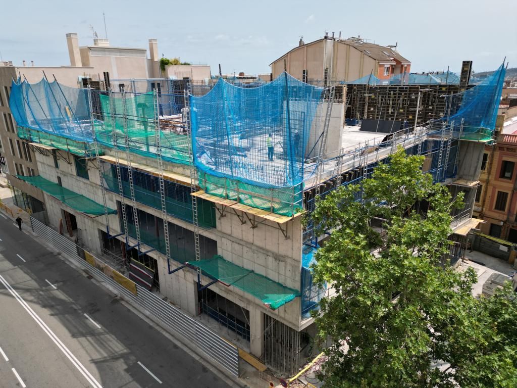 Edificio en construcción con red de seguridad azul y verde, paredes de hormigón y una ciudad de fondo.