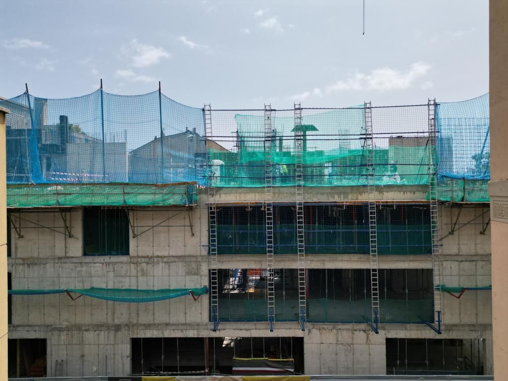 Obra de construcción con edificio de hormigón bajo andamios y redes de seguridad.