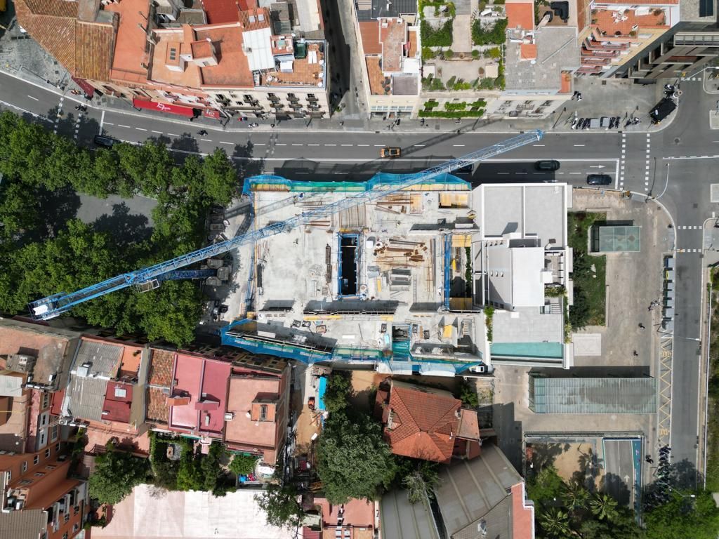 Vista aérea de un sitio de construcción con una grúa, rodeado de edificios y calles en una zona urbana.