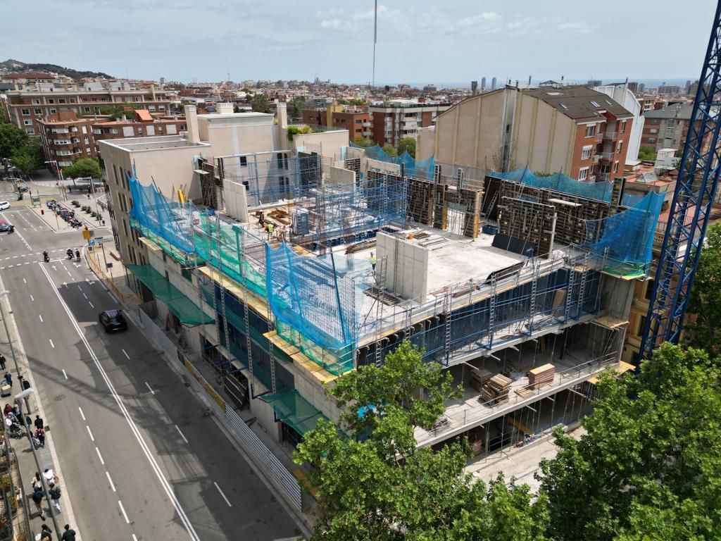 Obra: Estructura de un edificio de varias plantas con redes de seguridad. Calle y ciudad visibles al fondo.