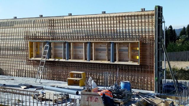 Obra en construcción, encofrado de hormigón con varillas de refuerzo, estructura de madera y abertura rectangular parcialmente construida, al aire libre en un día soleado.