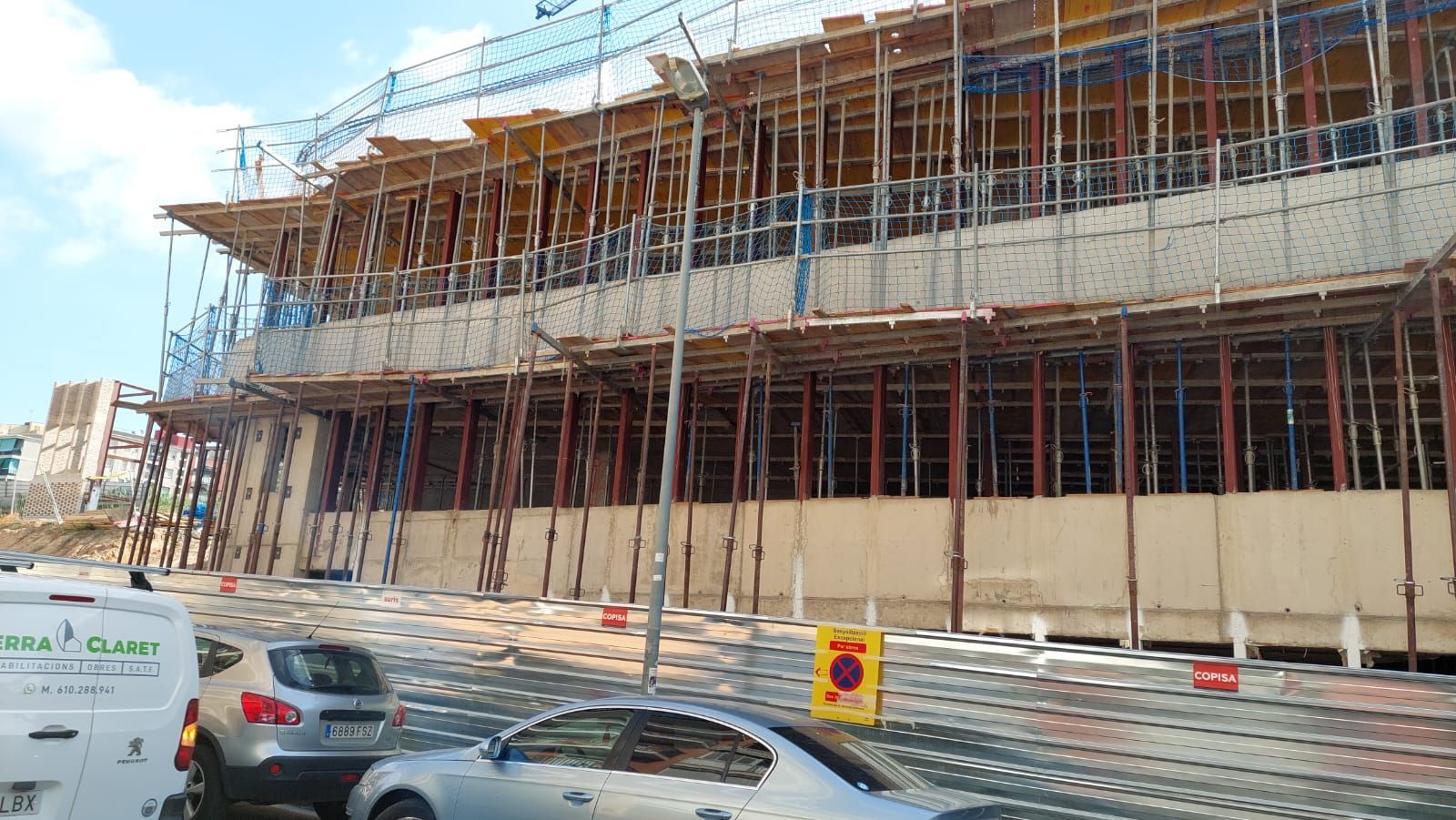 Sitio de construcción con andamios que sostienen la estructura del edificio; automóviles en la calle en primer plano.