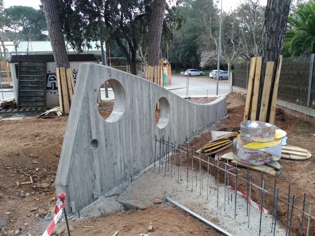 Muro de hormigón en construcción con agujeros circulares. Hay varillas de refuerzo y materiales de construcción. Exterior.