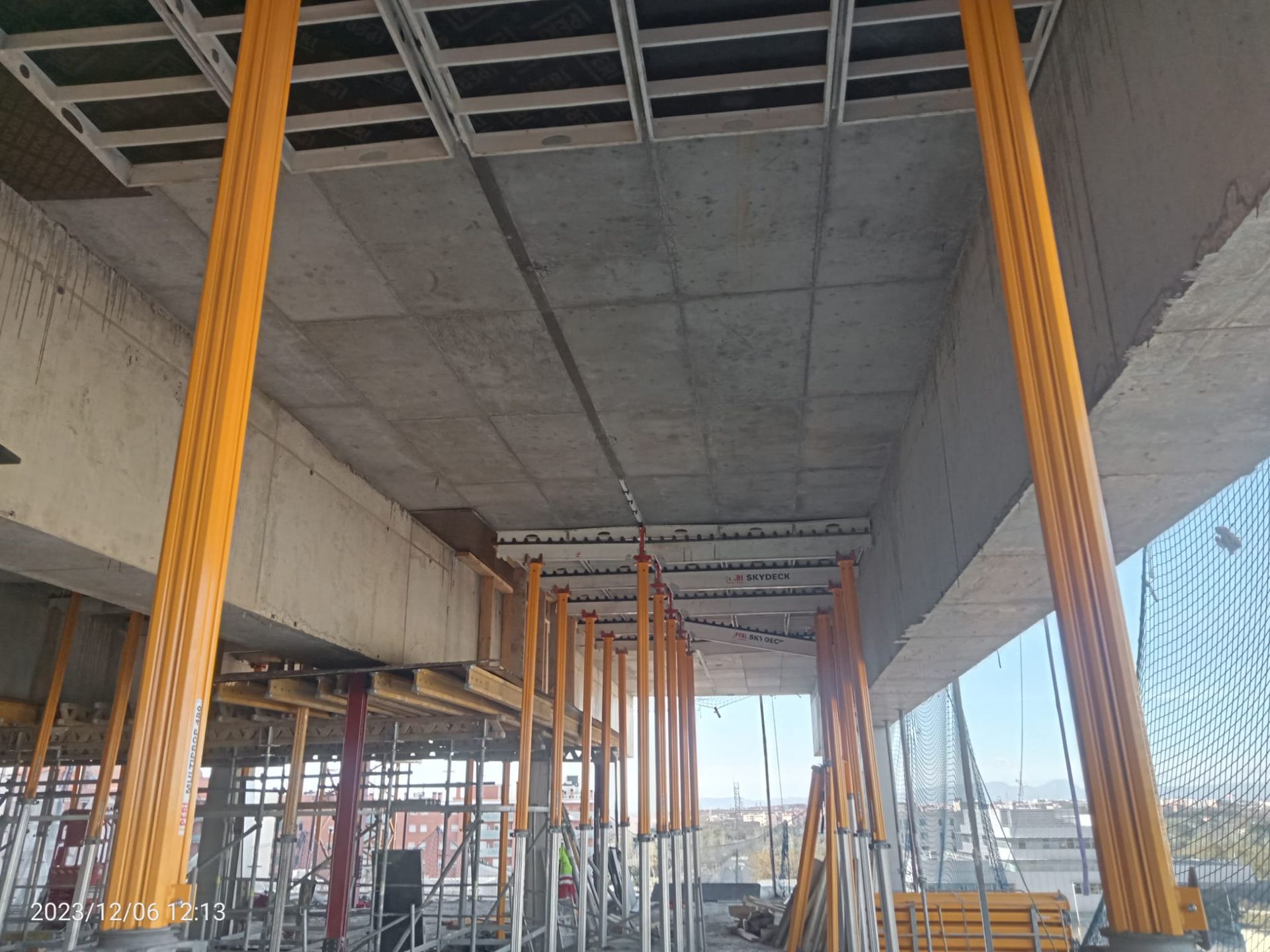 Obra en construcción con techo de hormigón sostenido por andamios amarillos.
