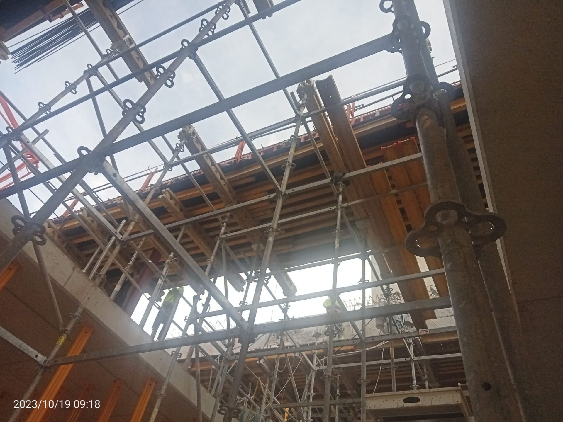 Andamios y encofrados de madera de color naranja en una obra en construcción, vista en ángulo contra un cielo nublado.