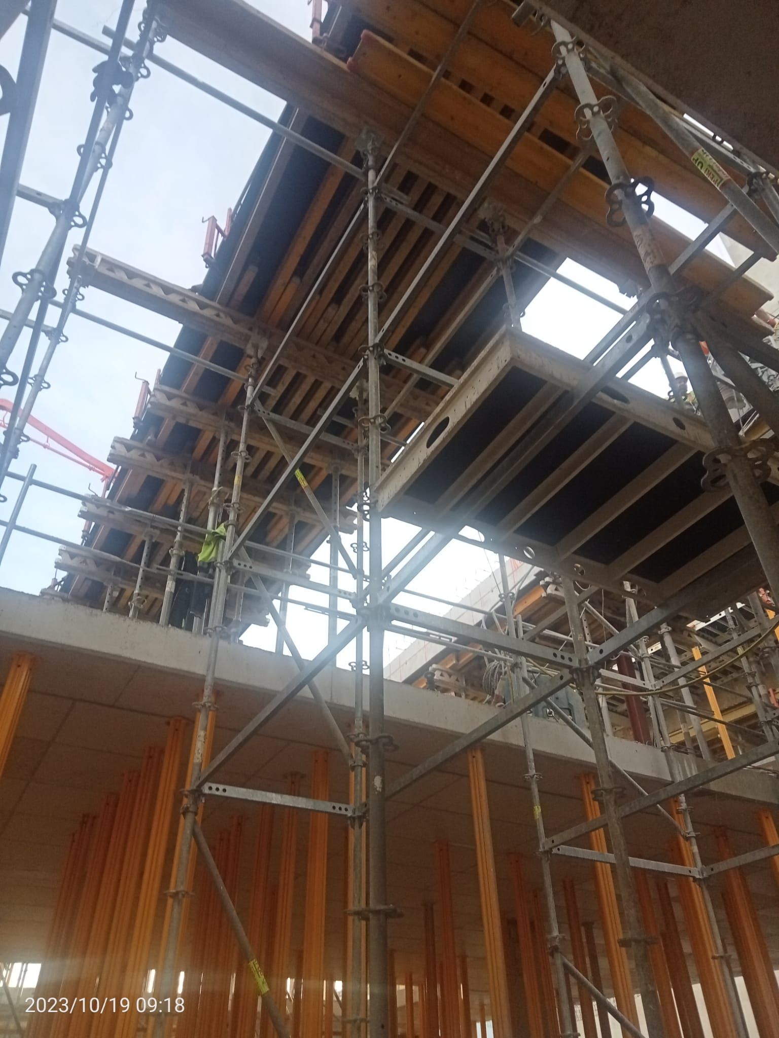 Obra de construcción con andamios que sostienen el encofrado de hormigón, trabajadores presentes.