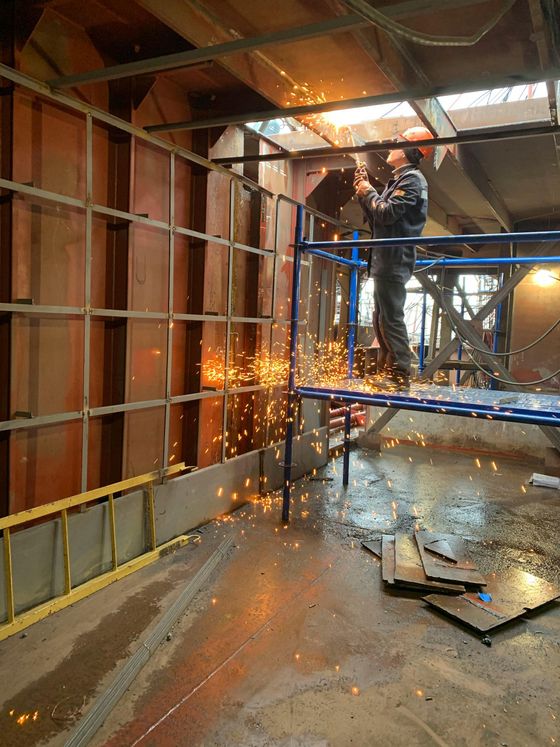 Soldador en un andamio, saltan chispas mientras trabaja en un marco de metal, en un entorno de construcción poco iluminado.