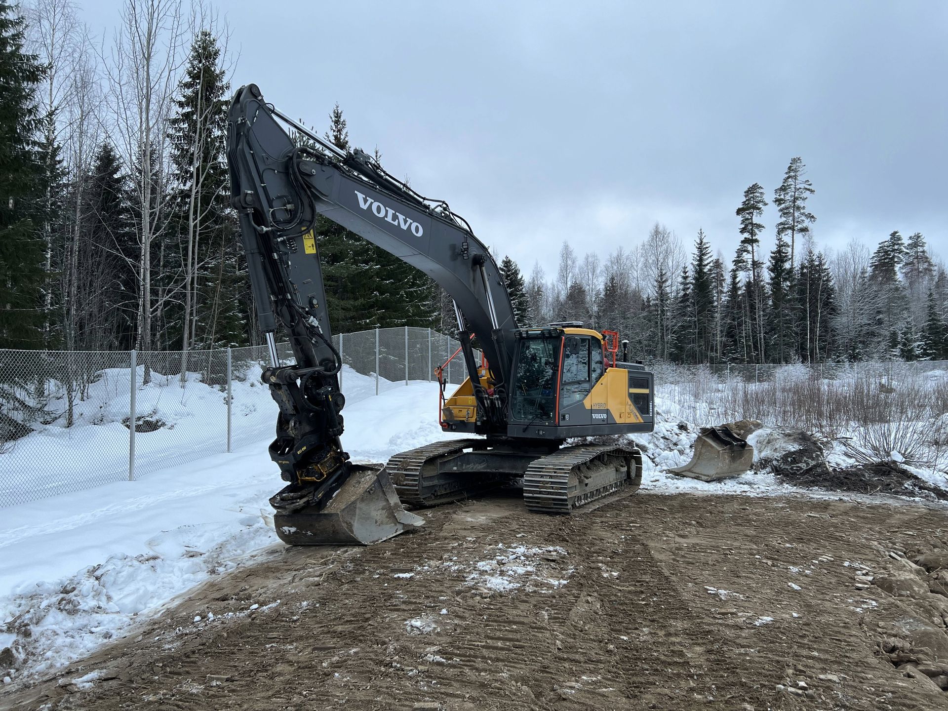 Musta Volvo-kaivinkone kaivaa mutaista aukiota sinisen taivaan alla