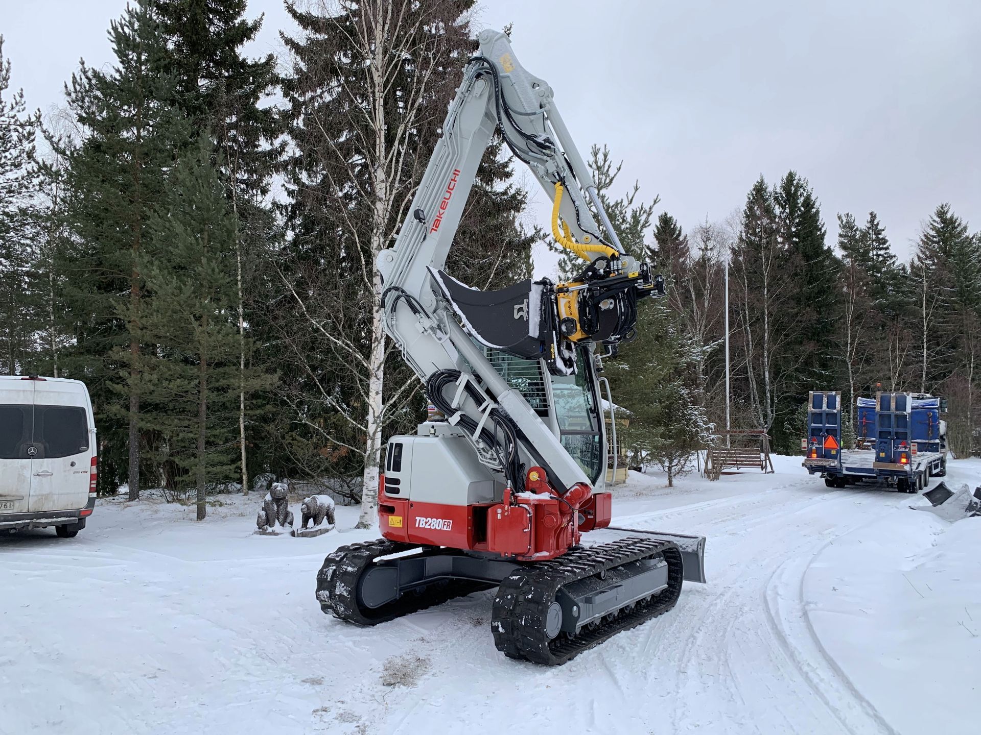 Minikaivuri tasoittamassa soraa rakenteilla olevan puutalon vieressä, taustalla toinen rakennus